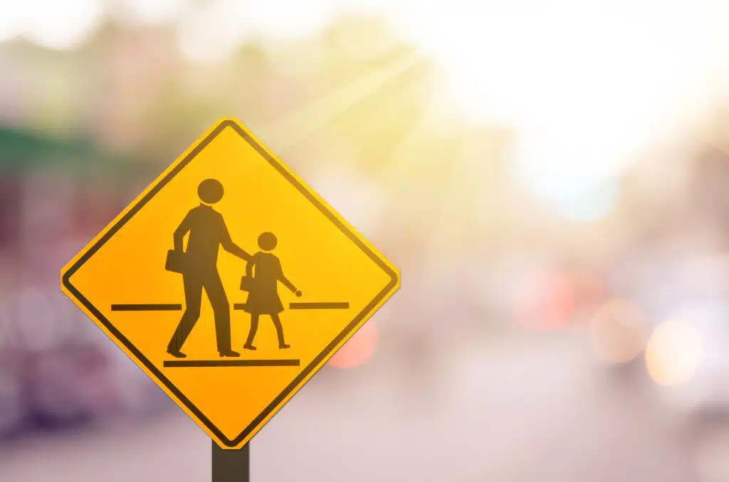 School zone warning sign on blur traffic road with colorful bokeh light abstract background. Copy space of transportation and travel concept. Vintage tone filter effect color style.